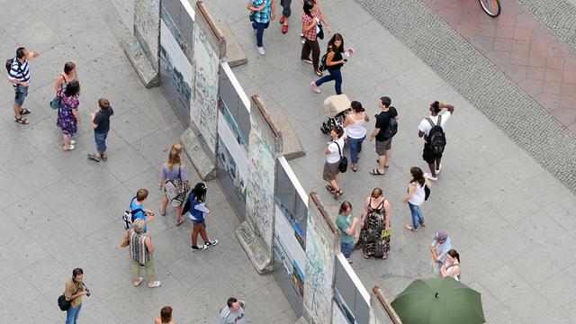 Besucher stehen auf beiden Seiten um einen historischen Teil der Berliner Mauer auf dem Potsdamer Platz herum.