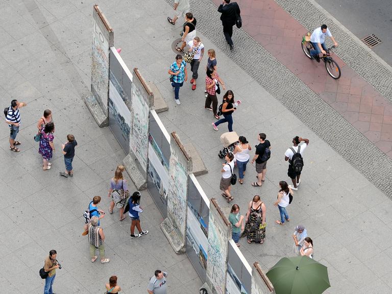 Besucher stehen auf beiden Seiten um einen historischen Teil der Berliner Mauer auf dem Potsdamer Platz herum.