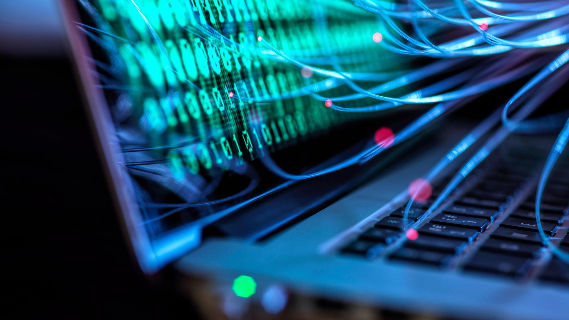 Illustration eines Laptops auf dessen Bildschirm Nullen und Einsen dargestellt sind. Lichtspuren führen auf die Tastatur und auf den Bildschirm des Laptops. (Symbolbild)