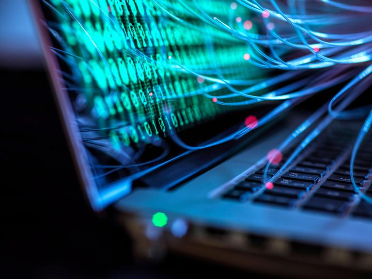 Illustration eines Laptops auf dessen Bildschirm Nullen und Einsen dargestellt sind. Lichtspuren führen auf die Tastatur und auf den Bildschirm des Laptops. (Symbolbild)