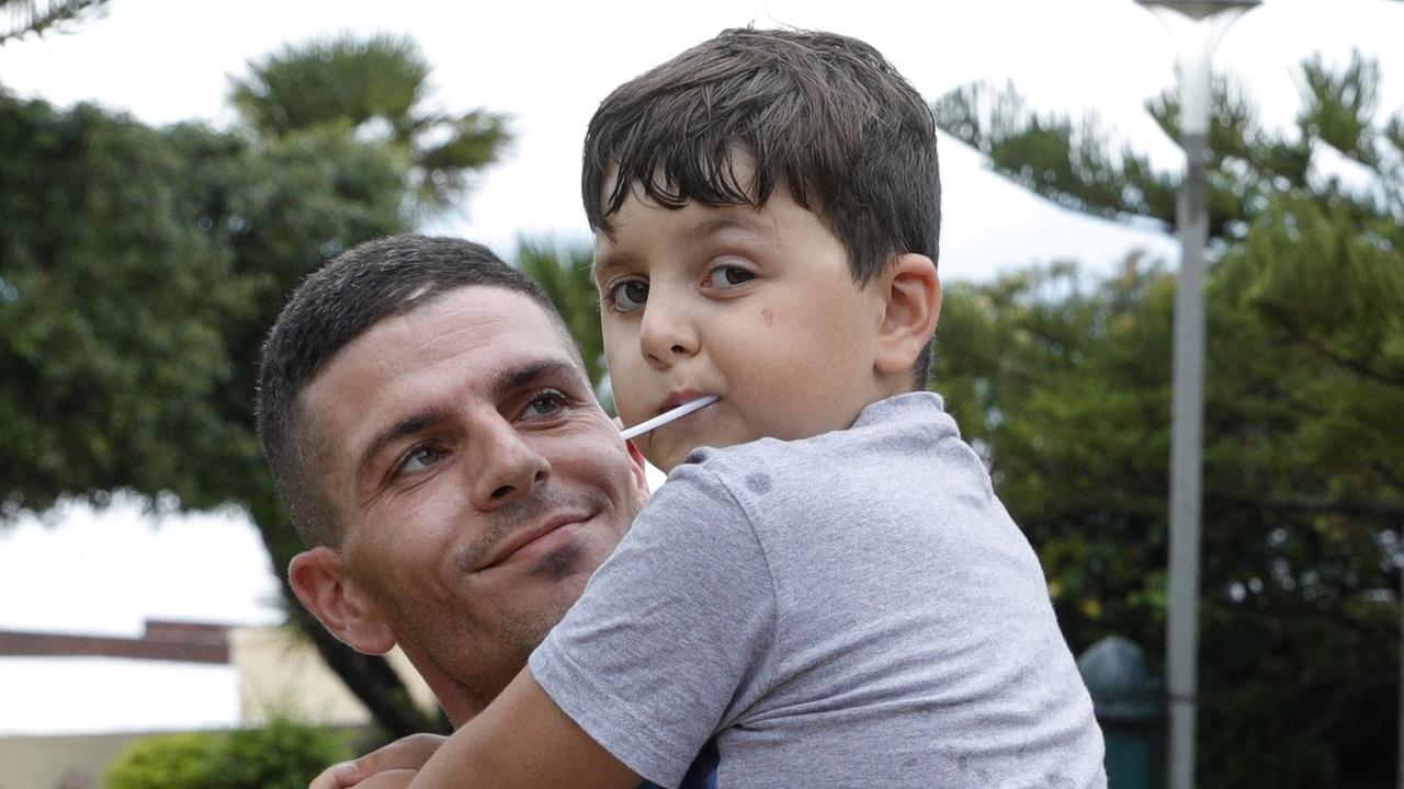 Korsika: Kenzo, ein 8-jähriger krebskranker Junge und Olympique-Marseille-Fan hat einen Lutscher im Mund und wird von seinem Vater auf den Armen gehalten.