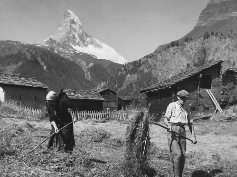 Mann und Frau bei der Heuernte in den Schweizer Bergen, im Hintergrund ist das Matterhorn zu sehen, ca. 1930.