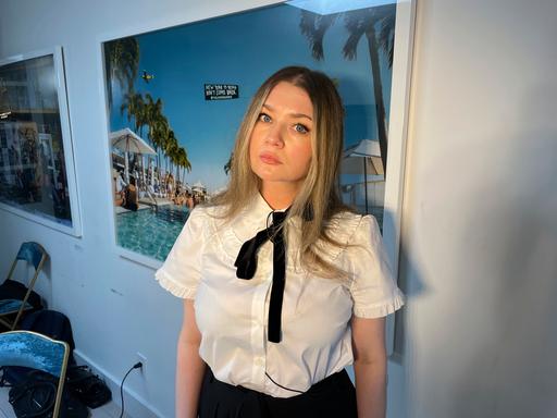 Anna Delvey possiert vor einem Foto und guckt in die Kamera.