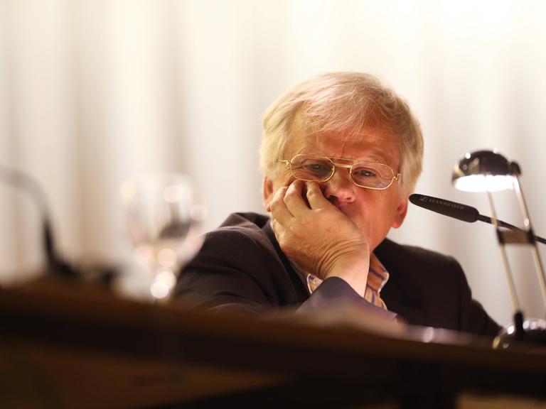 Der Schweizer Philosoph und Literat Peter Bieri alias Pascal Mercier sitzt im Anzug vor einem Tisch mit Mikrofon, er hat das Kinn in die Hand gestützt und blickt nachdenklich vor sich hin.