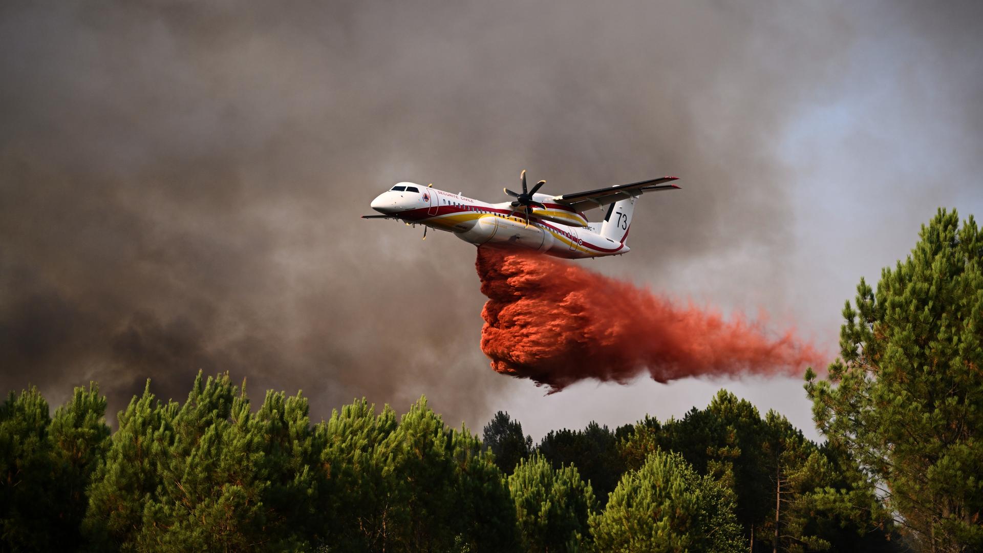 Ein Flugzeug versprüht rotfarbenes Löschmittel über einem brennenden Wald. Ein Flugzeug versprüht rotfarbenes Löschmittel über einem brennenden Wald.