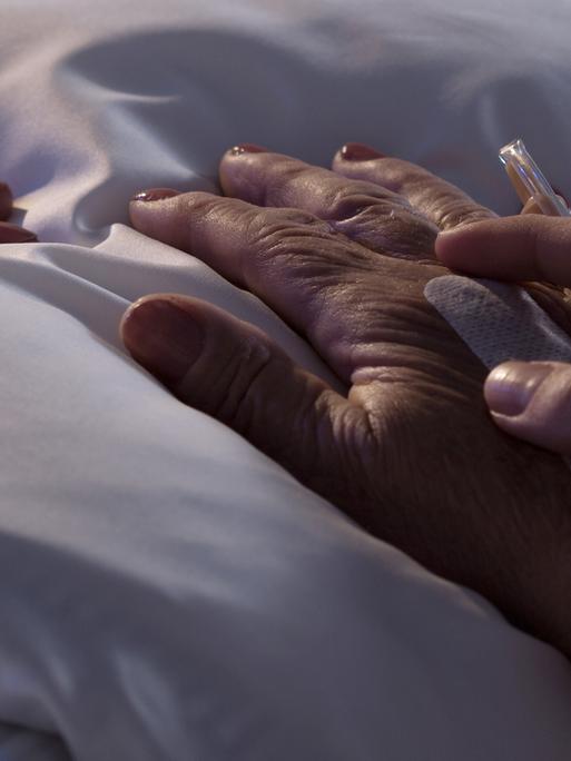 Einem sterbenden Menschen wird die Hand gehalten an einem Krankenhausbett.