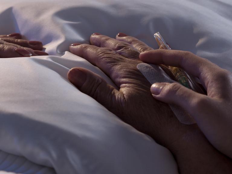 Einem sterbenden Menschen wird die Hand gehalten an einem Krankenhausbett.