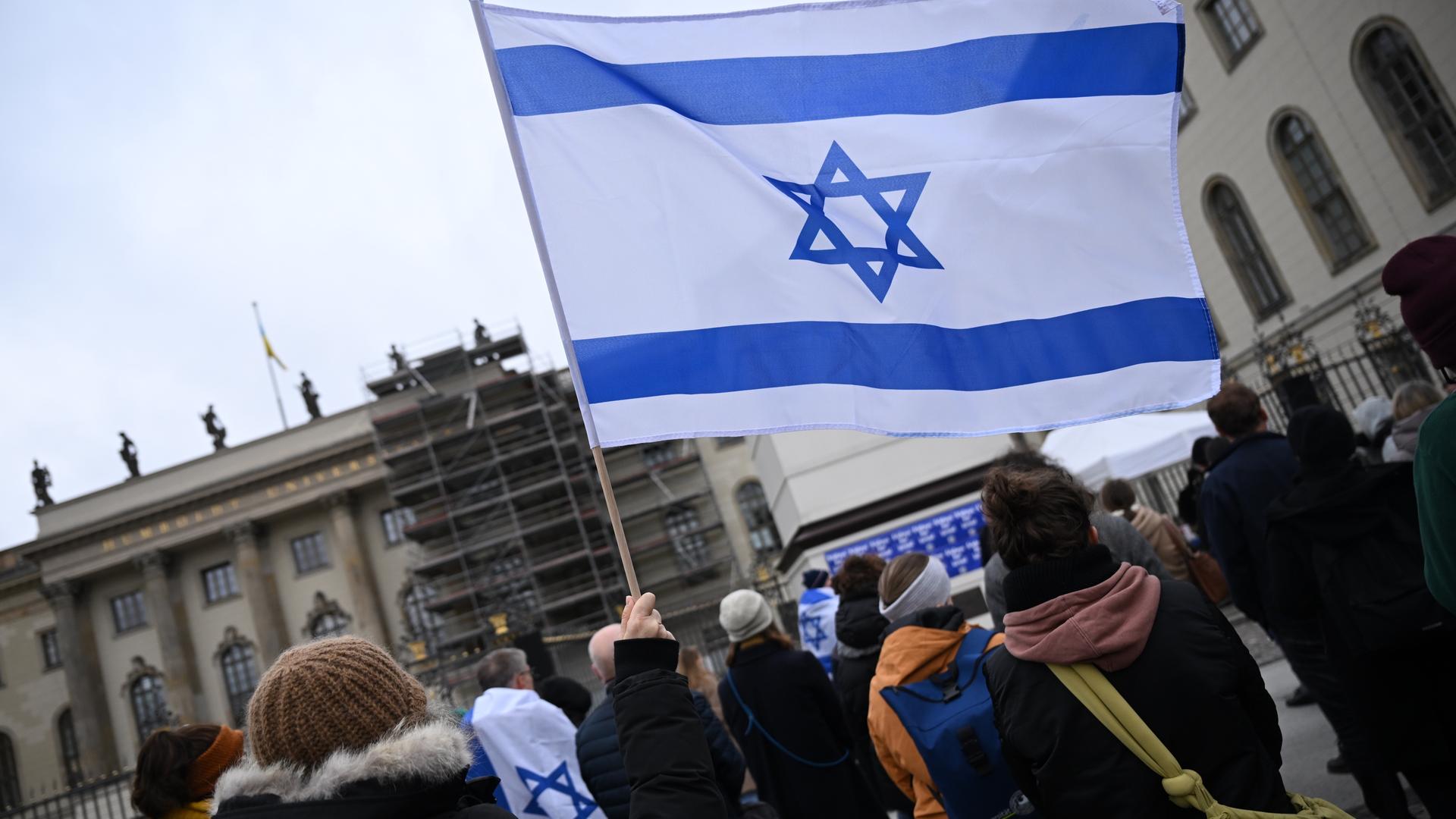 Mehrere Menschen stehen vor einem Universitätsgebäude. Eine Israel-Flagge wird in die Höhe gehalten. Mehrere Menschen stehen vor einem Universitätsgebäude. Eine Israel-Flagge wird in die Höhe gehalten.