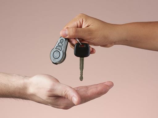 Ein Autoschlüssel wird von einer Hand in die andere gegeben.