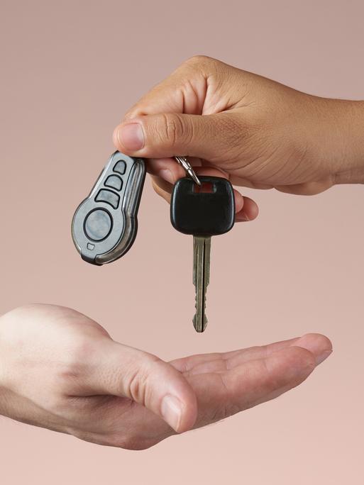 Ein Autoschlüssel wird von einer Hand in die andere gegeben.