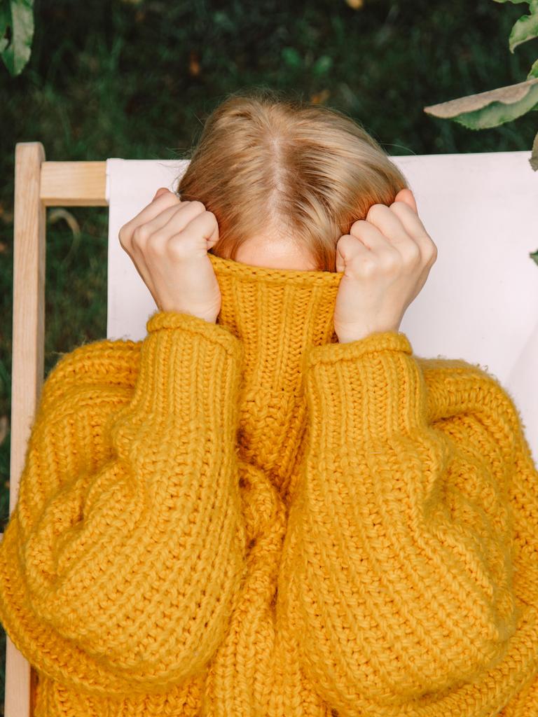 Eine Frau in gelbem Pullover versteckt ihr Gesicht im hochgezogenen Pulloverkragen.