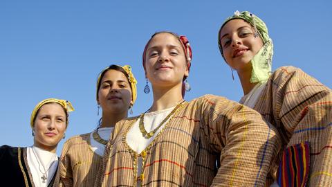 Vier junge Frauen in traditionellen, zyprischen Kleidern stehen in Limassol beieinander und lächeln in die Kamera.
