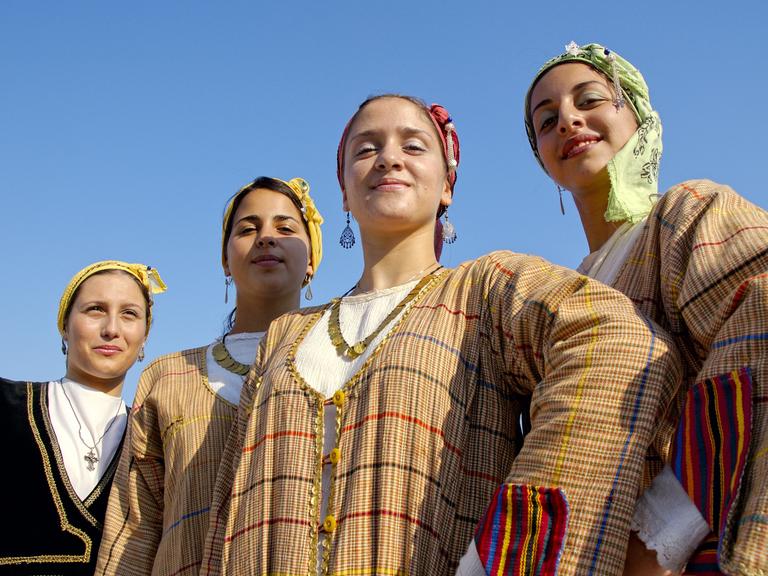 Vier junge Frauen in traditionellen, zyprischen Kleidern stehen in Limassol beieinander und lächeln in die Kamera.