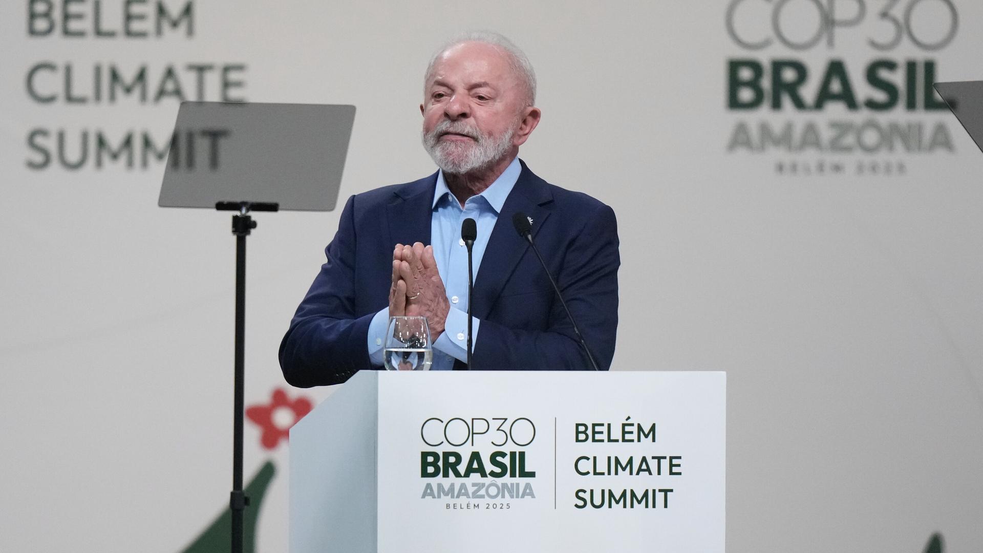 Lula steht an einem Rednerpult und faltet bittend die Hände zusammen. Auf dem Pult und an einer hellen Wand dahinter prangen die Schriftzüge des Weltklimagipfels. 