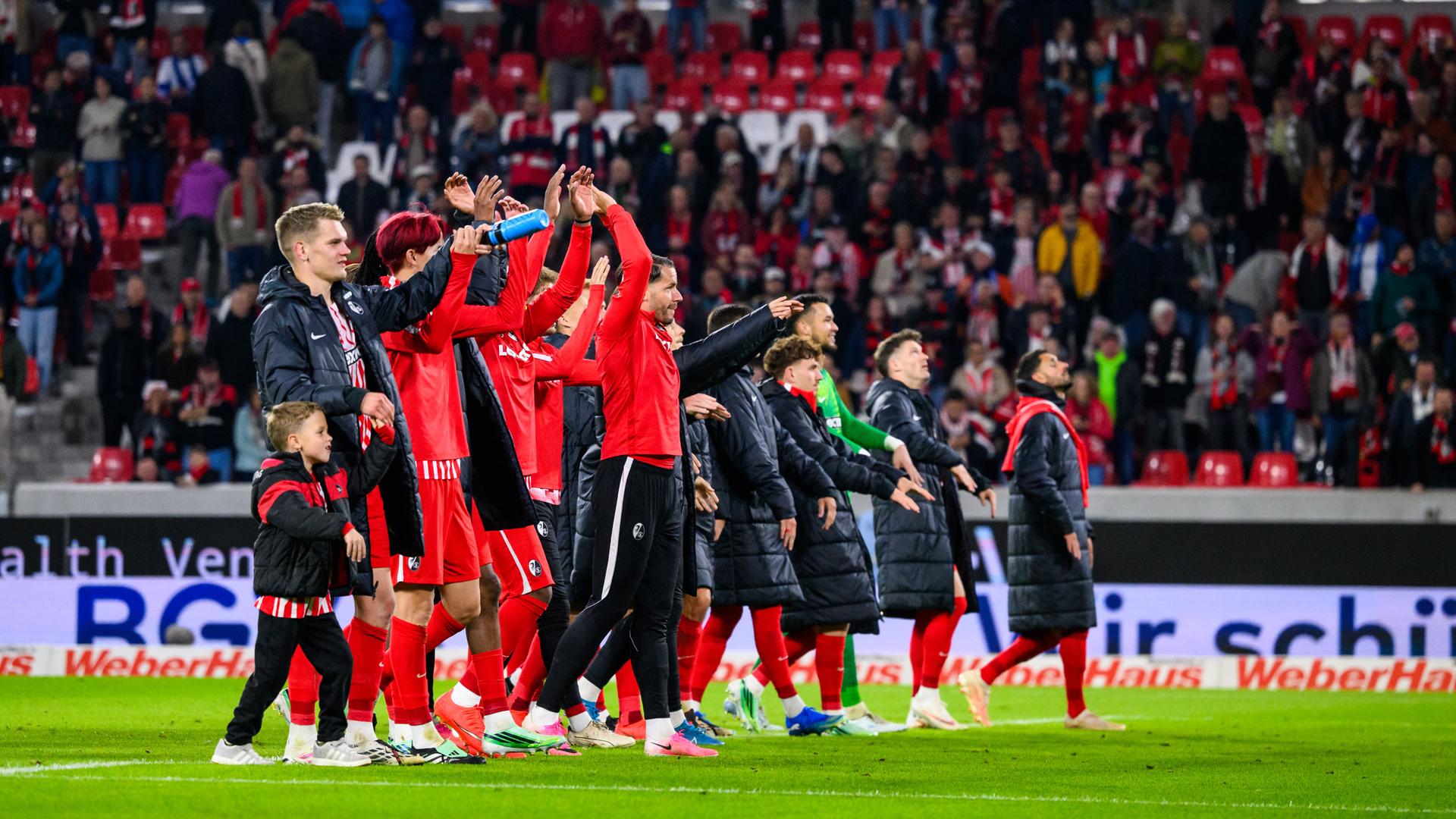 Die Spieler des SC Freiburg jubeln nach dem Spiel über den Sieg und bedanken sich mit einer La-Ola-Welle bei den Fans für die Unterstützung.
