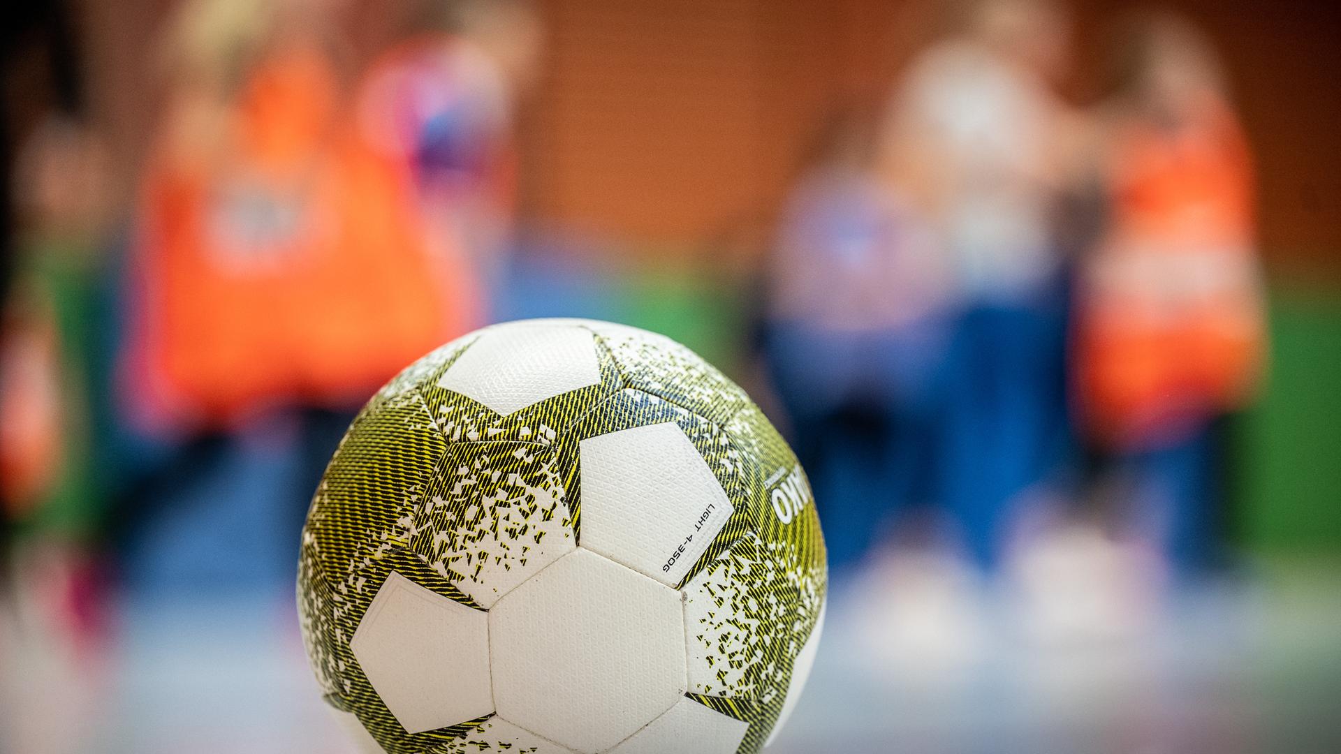 Ein Fußball in einer Schulturnhalle mit Kindern im Hintergrund.