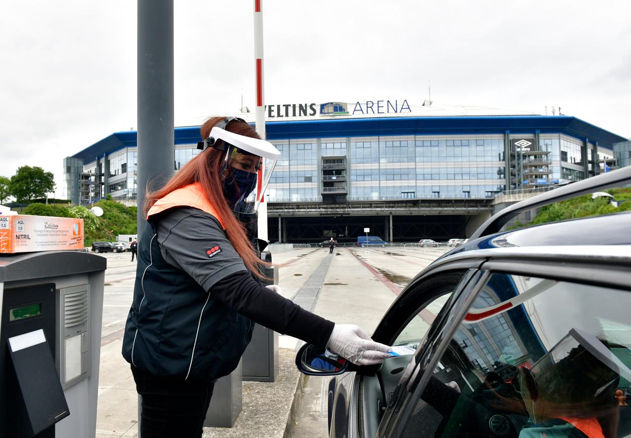 Ein Steward kontrolliert mit Gesichtsschutz und mit medizinischem Mundschutz vor der Veltins-Arena vor dem Spiel Tickets.