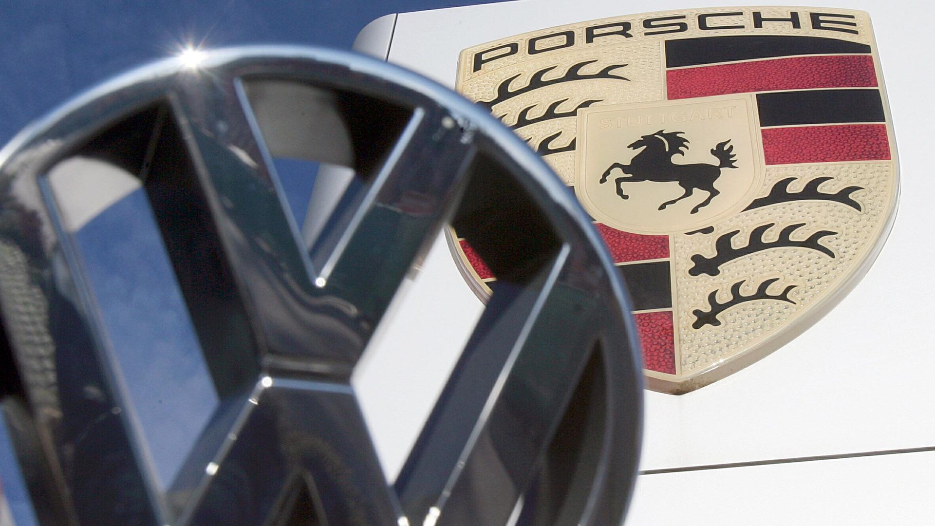 Ein VW-Logo ist vor einem Porsche-Firmenlogo vor dem Porsche Center in Stuttgart-Zuffenhausen zu sehen.