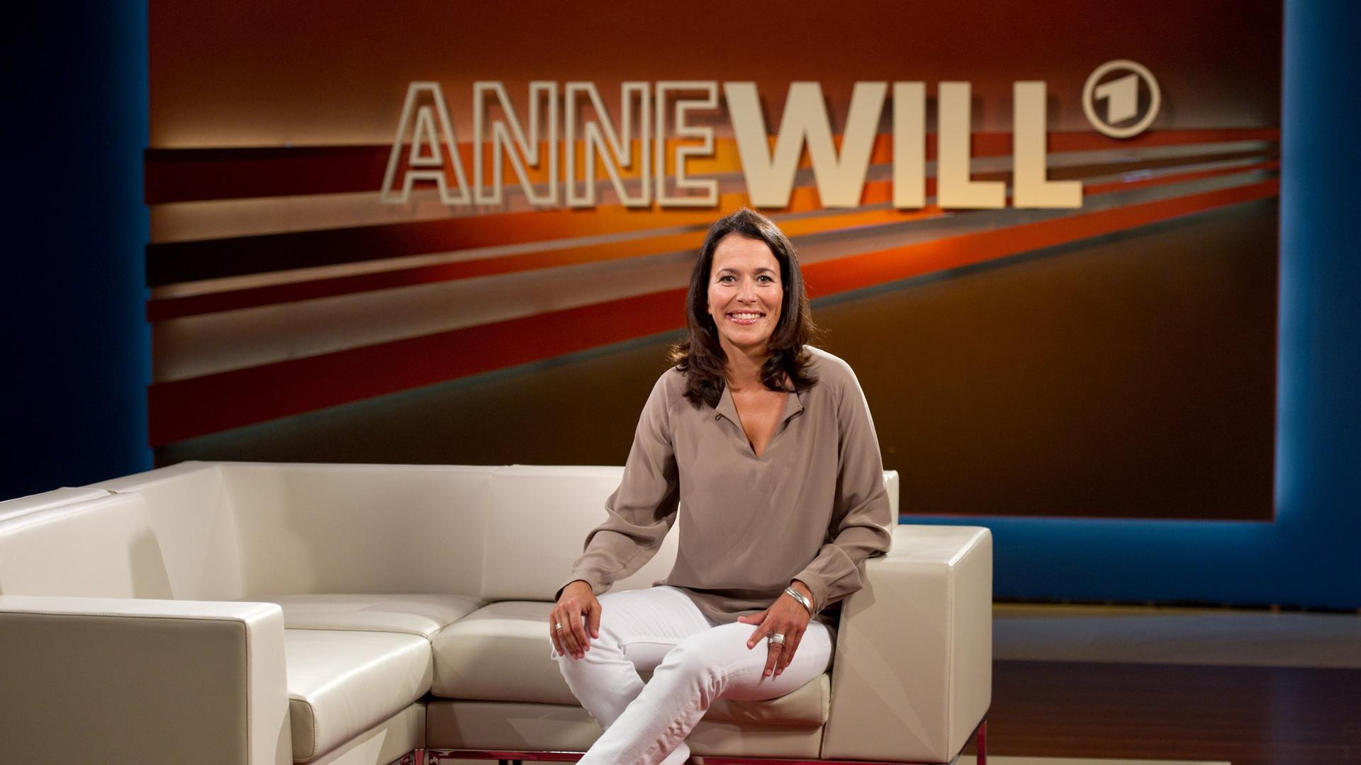 Die Moderatorin und Journalistin Anne Will sitzt auf einer Couch in ihrem Studio.