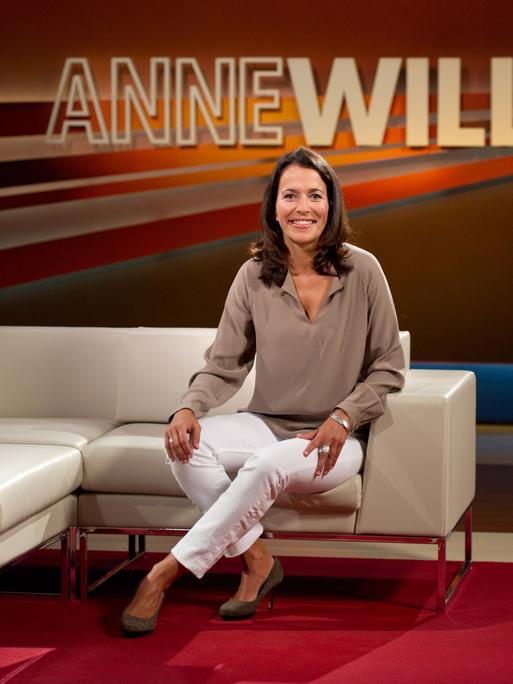 Die Moderatorin und Journalistin Anne Will sitzt auf einer Couch in ihrem Studio.