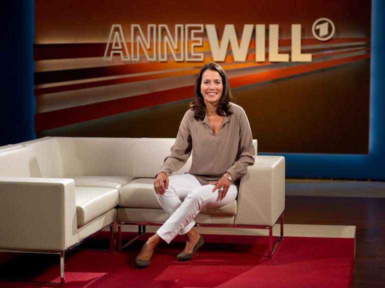 Die Moderatorin und Journalistin Anne Will sitzt auf einer Couch in ihrem Studio.