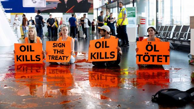 Klima-Aktivisten sitzen im Flug-Hafen Wien auf dem Boden. Sie halten Plakate, auf dem Boden ist Farbe ausgeschüttet. 