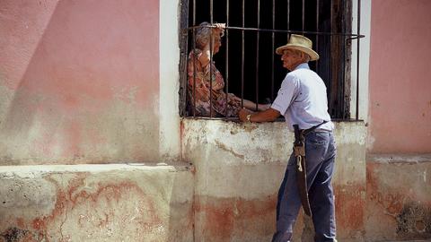 Straßenszene in Kubas Hauptstadt Havanna: Ein alter Mann im Gespräch mit einer alten Frau, die hinter einem vergitterten Fenster sitzt.