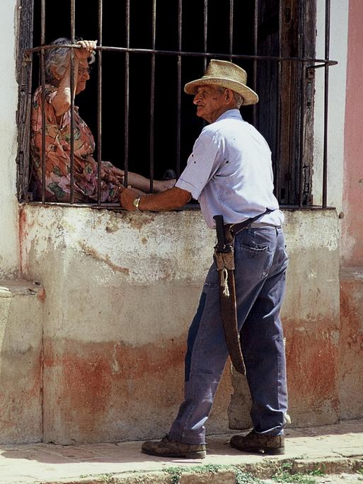 Straßenszene in Kubas Hauptstadt Havanna: Ein alter Mann im Gespräch mit einer alten Frau, die hinter einem vergitterten Fenster sitzt.