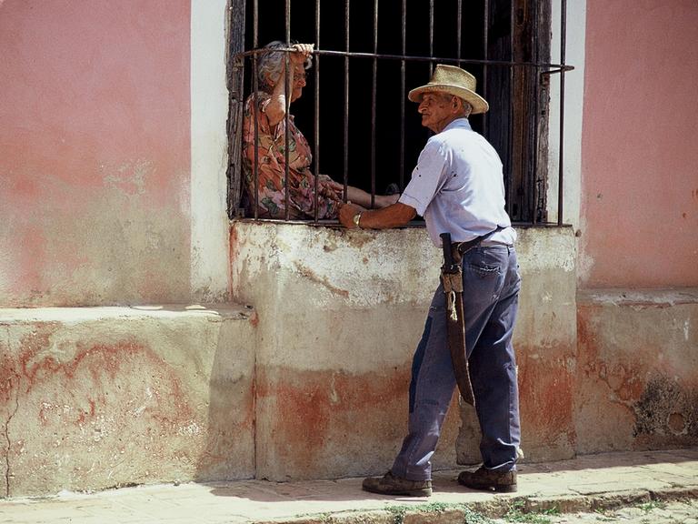 Straßenszene in Kubas Hauptstadt Havanna: Ein alter Mann im Gespräch mit einer alten Frau, die hinter einem vergitterten Fenster sitzt.