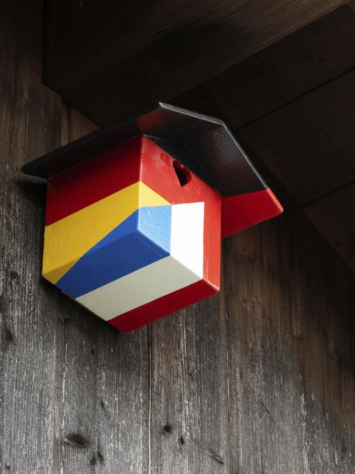 Ein Nistkasten für Vögel in den Farben der deutschen und französischen Nationalflagge hängt an einer hölzernen Hauswand. Ein Nistkasten für Vögel in den Farben der deutschen und französischen Nationalflagge hängt an einer hölzernen Hauswand.