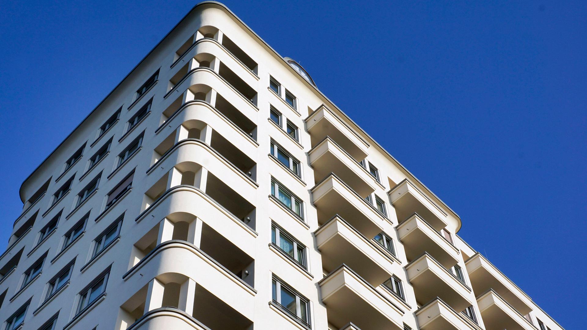 Blick nach oben auf ein Wohnhaus mit Balkonen vor einem blauen Himmel.