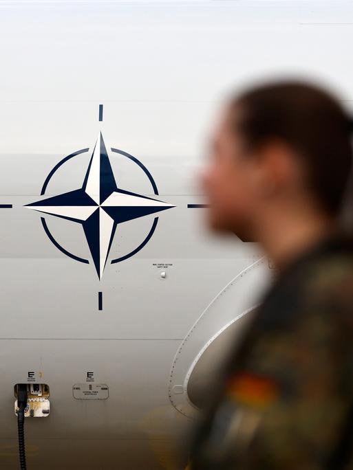 Eine Soldatin steht vor einem NATO-Logo. Das Logo ist auf einem AWACS-Flugzeug angebracht. Eine Soldatin steht vor einem NATO-Logo. Das Logo ist auf einem AWACS-Flugzeug angebracht.