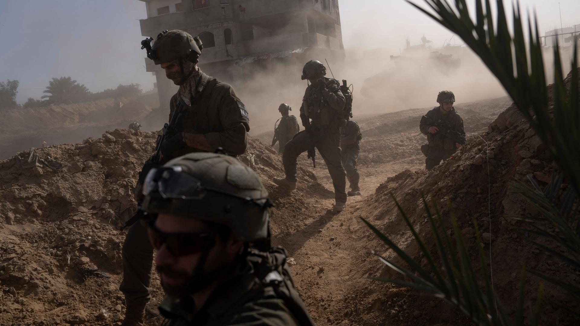 Israelische Soldaten stehen in einer verstaubten Umgebung vor einem großen Haus.
