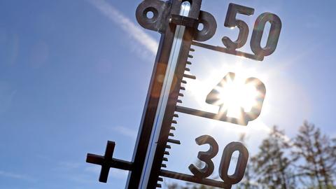 Ein Thermometer vor blauem Himmel und der Sonne.