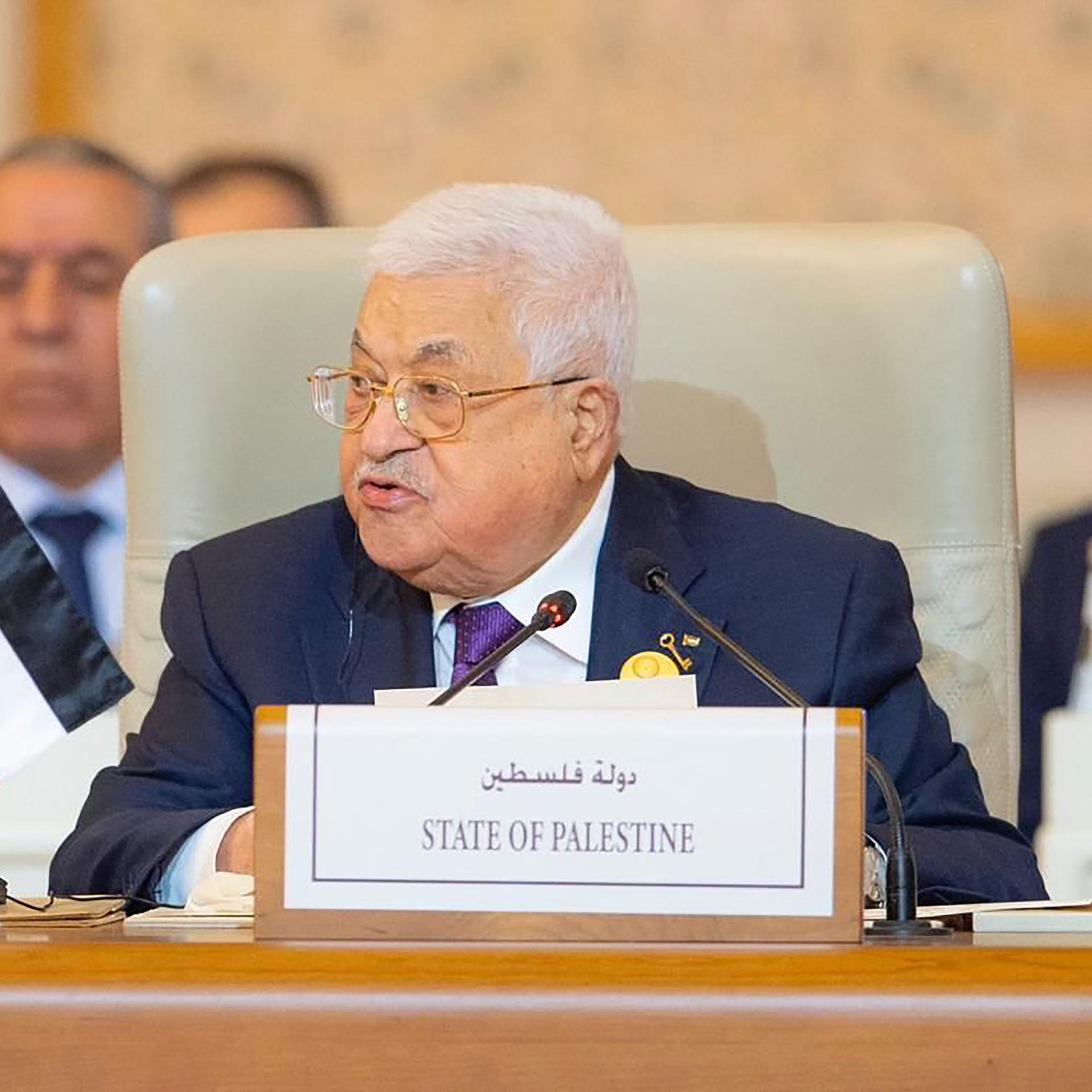 Mahmoud Abbas bei einem Notfallmeeting der Arabischen Liga. Er sitzt an einem Konferenztisch, auf dem Schild vor ihm steht auf Englisch und Arabisch "State of Palestine". Er schaut leicht zur Seite.