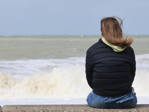 Frau sitzt auf einer Mauer und schaut aufs in Mers les Bains im Norden Frankreichs.