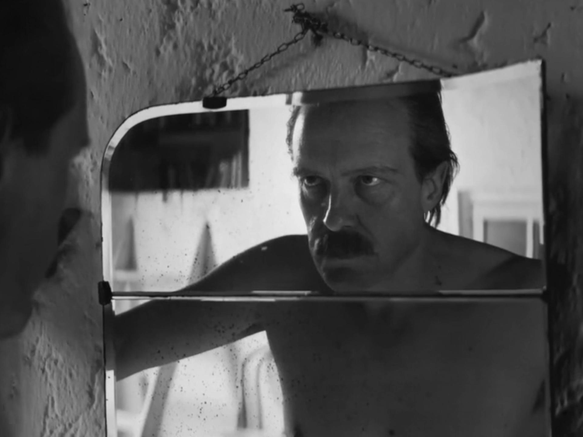 Schauspieler August Diehl schaut in der Figur des Josef Mengele in einer Filmszene in einen Spiegel und betrachtet sein Gesicht. 