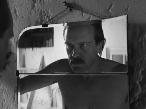 Schauspieler August Diehl schaut in der Figur des Josef Mengele in einer Filmszene in einen Spiegel und betrachtet sein Gesicht. 