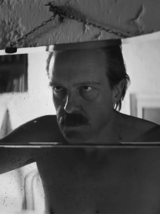 Schauspieler August Diehl schaut in der Figur des Josef Mengele in einer Filmszene in einen Spiegel und betrachtet sein Gesicht. 