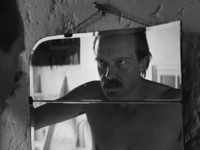 Schauspieler August Diehl schaut in der Figur des Josef Mengele in einer Filmszene in einen Spiegel und betrachtet sein Gesicht. 