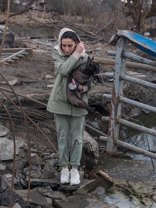 Eine junge Frau versucht mit einem Hund in den Armen einen Fluss zu überqueren.