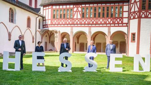Vier Männer und eine Frau stehen auf einer Rasenläche hinter großen weißen Buchstaben, die das Wort "Hessen"  bilden.