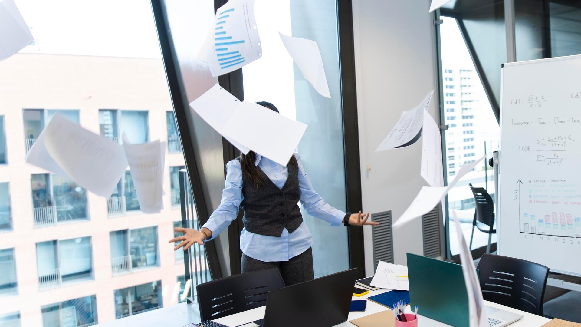 Gestresster Manager, der mit Papier um sich wirft in einem modernen Büro. 