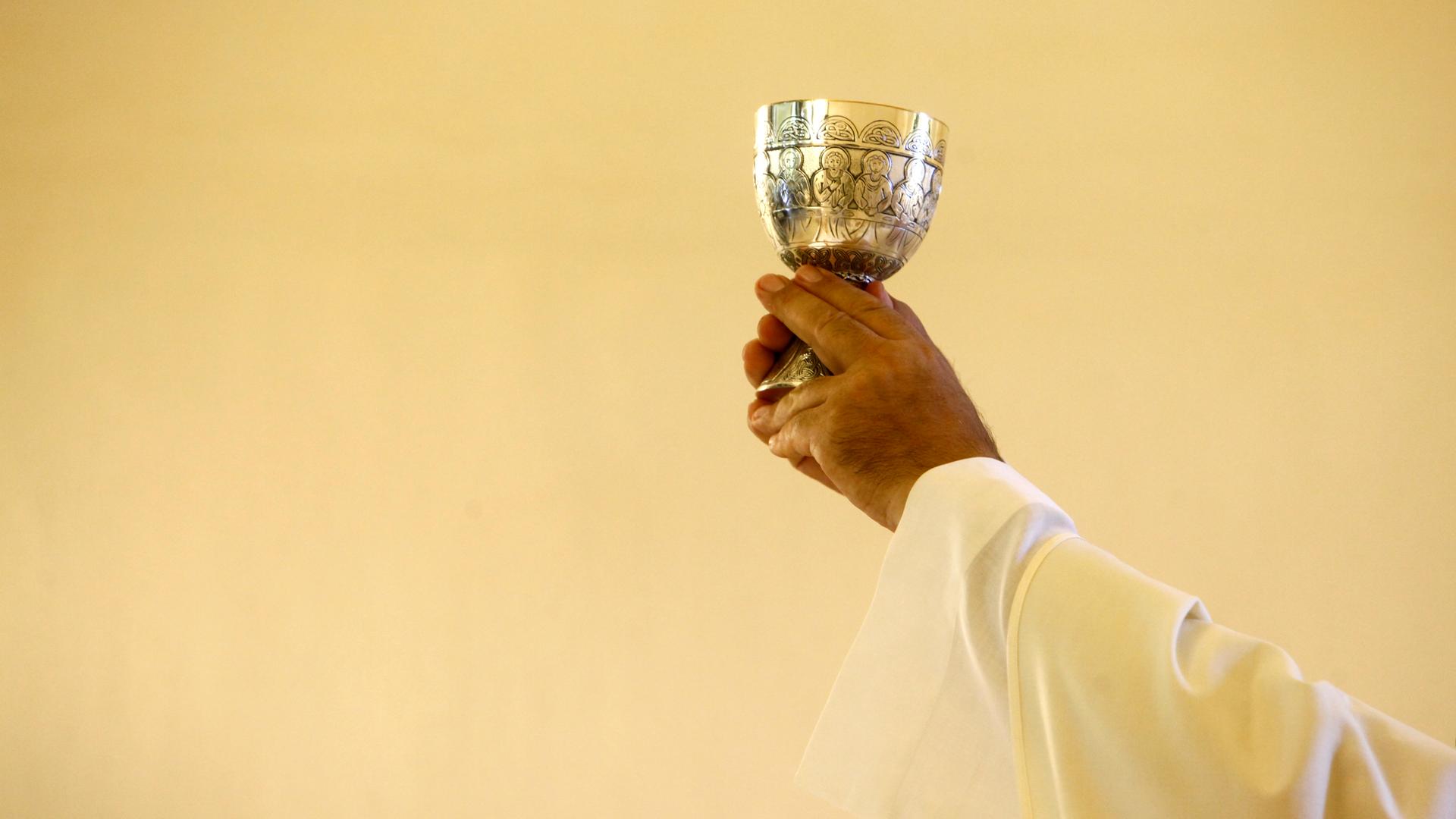 Eine Person in Ordenskleidung hält einen Abendsmahlkelch in die Luft.