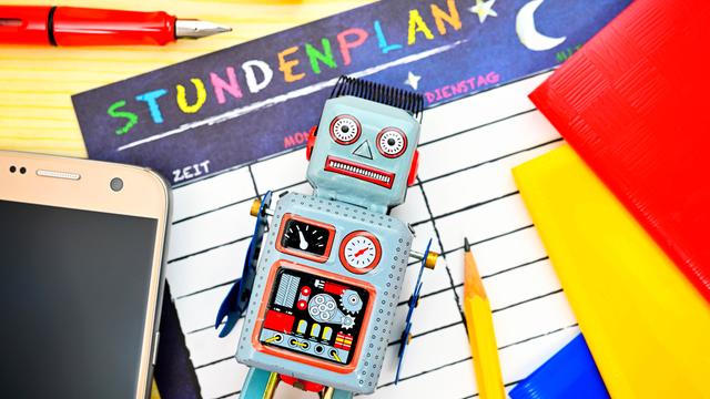 Roboter umgeben von Schulutensilien, Symbolfoto für das Erlernen von KI-Umgang in der Schule