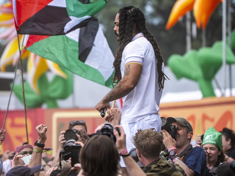 Der Musiker Bob Vylan auf der Bühne des Glastonbury Festivals. Im Hintergrund sind palästinensische Flaggen zu sehen. 