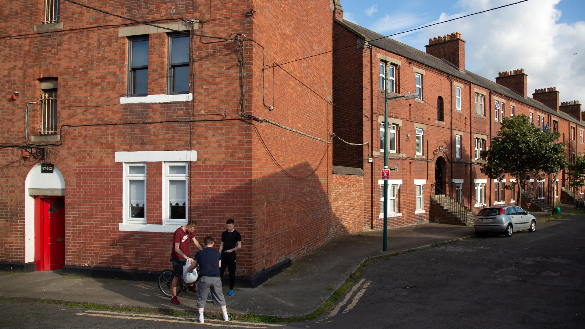 Jugendliche stehen zusammen auf einer Straße vor einer Häuserreihe ehemaliger Arbeitersiedlungen in Dublin. 