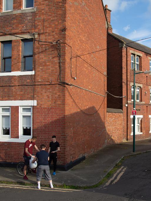 Jugendliche stehen zusammen auf einer Straße vor einer Häuserreihe ehemaliger Arbeitersiedlungen in Dublin. 