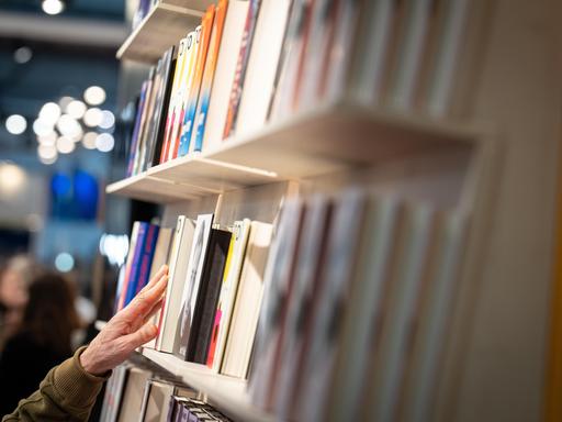 Impressionen von der Leipziger Buchmesse 2026: Eine Hand fasst an ein Buch, das in einem Regal steht Impressionen von der Leipziger Buchmesse 2026: Eine Hand fasst an ein Buch, das in einem Regal steht