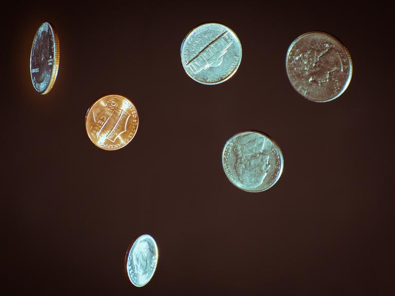 Vereinzelt schwebende oder fallende Münzen vor einem schwarzen Hintergrund